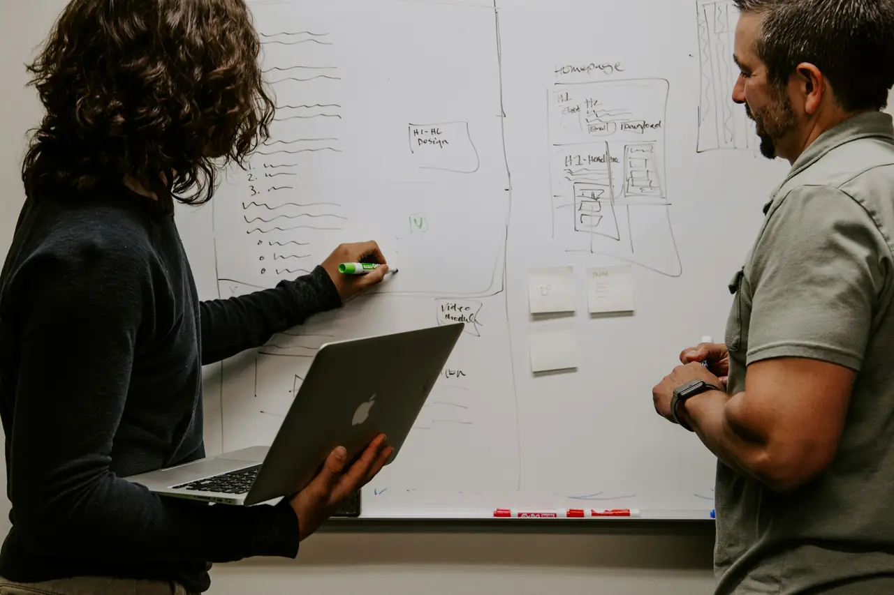 Deux personnes devant un tableau blanc, ordinateur portable en main
